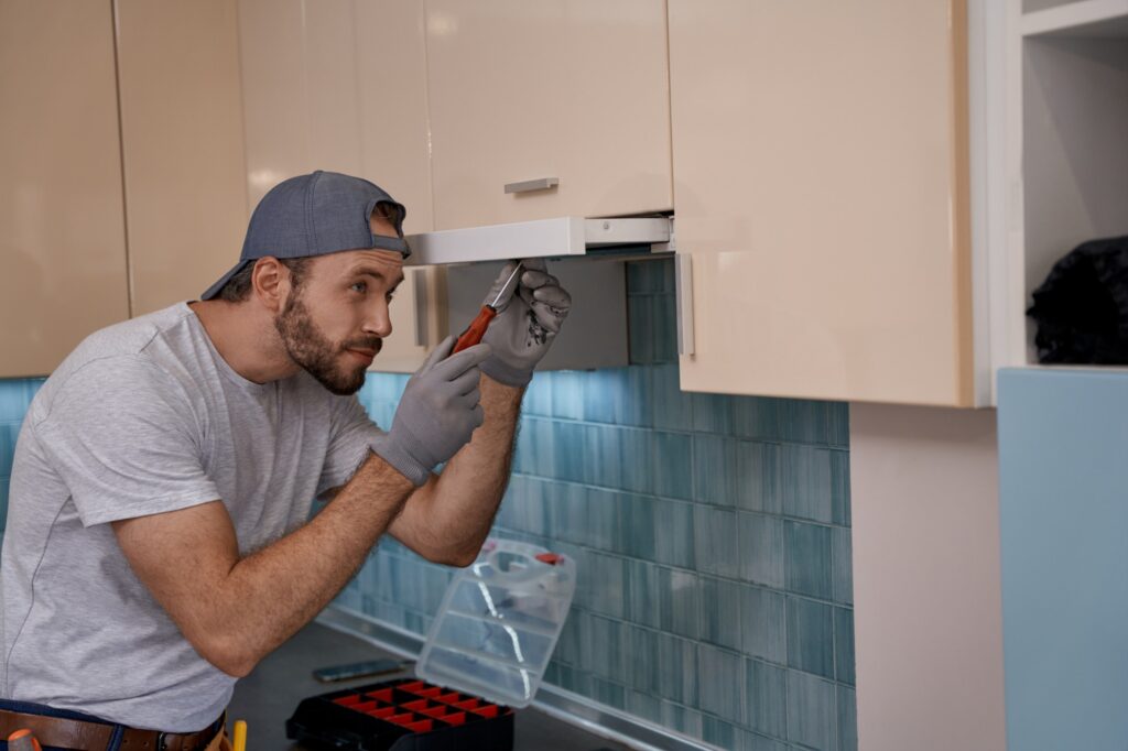 Young caucasian repairman installing kitchen hood using screwdriver